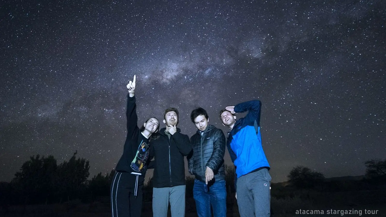 A group standing beside a telescope under a star-filled desert sky