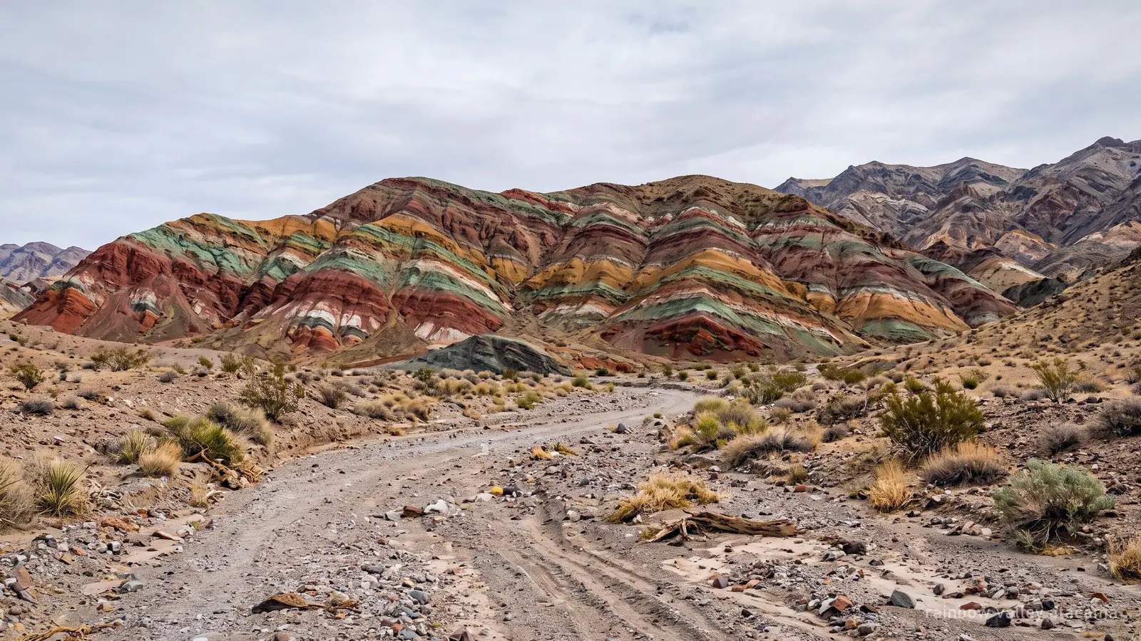 Desert hills banded in green, rust and white mineral layers under flat midday light