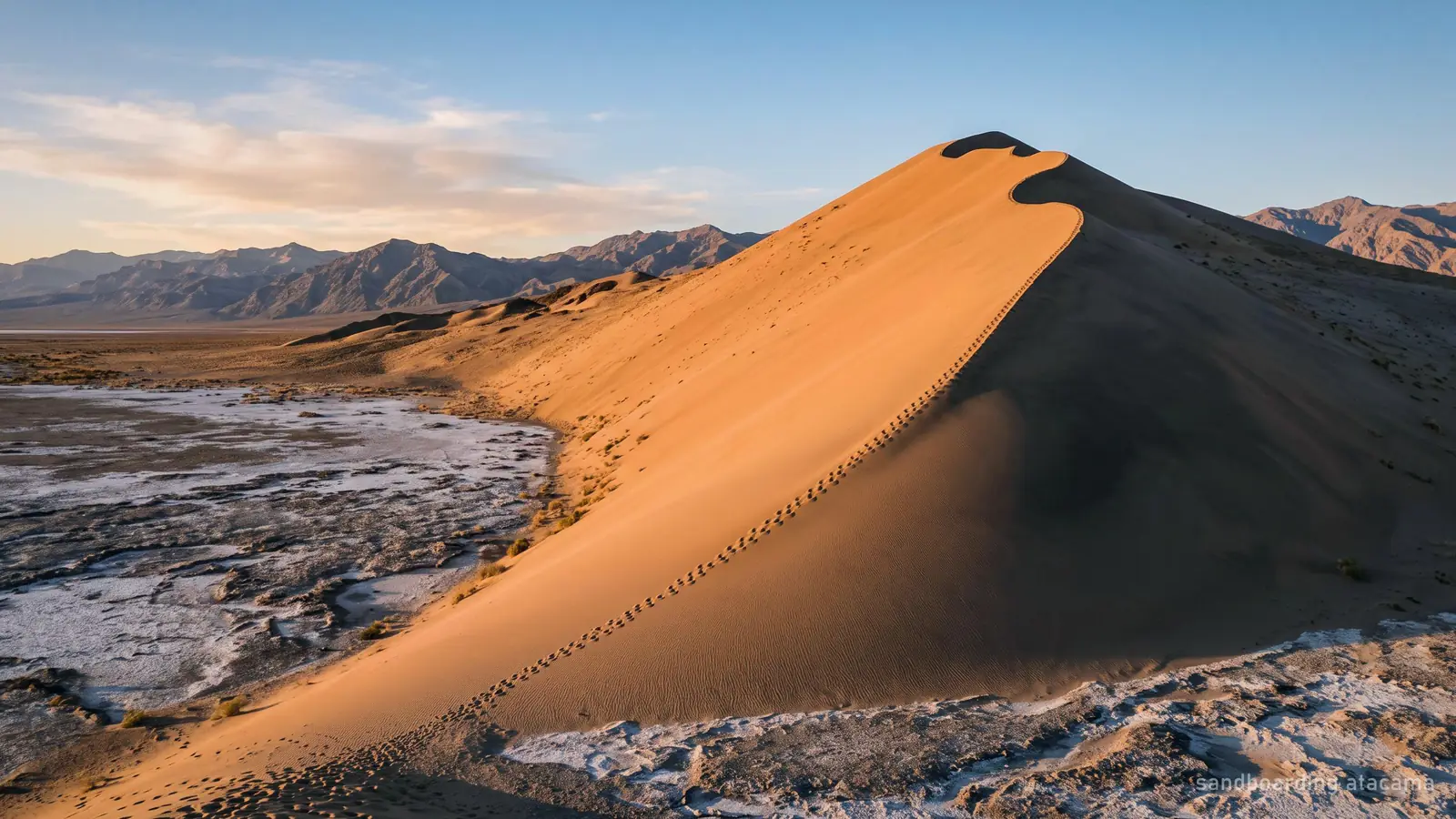 A sandboarder riding down a steep desert dune