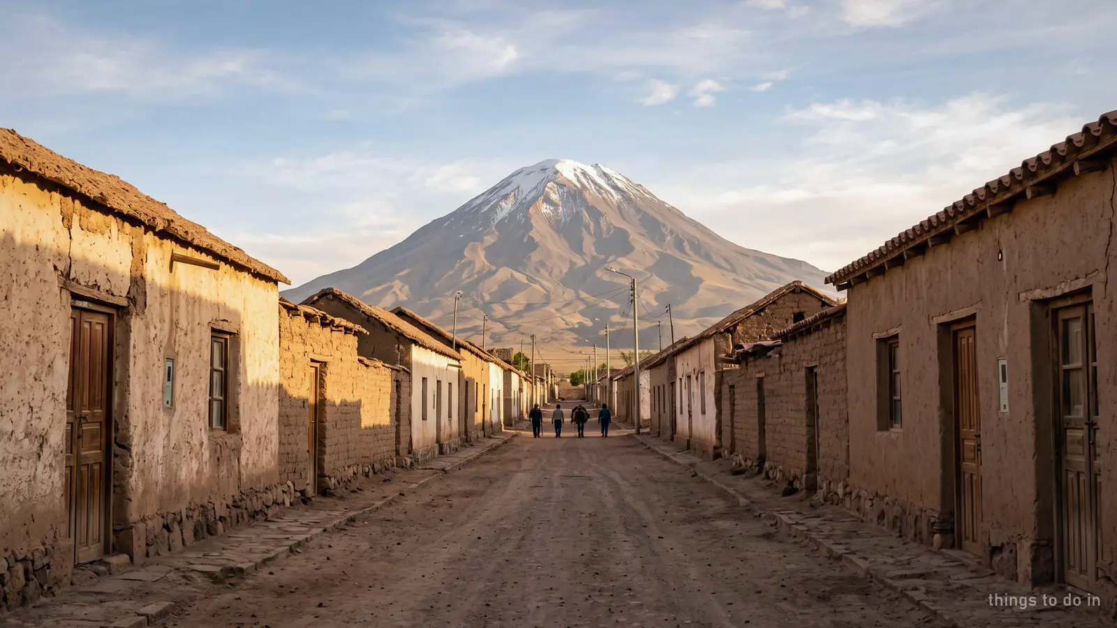 A low adobe street with a volcano rising behind the rooftops at the end of it