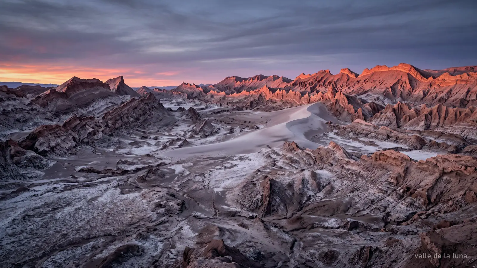 An eroded salt and clay valley at dusk, ridgelines turning orange against a dark sky